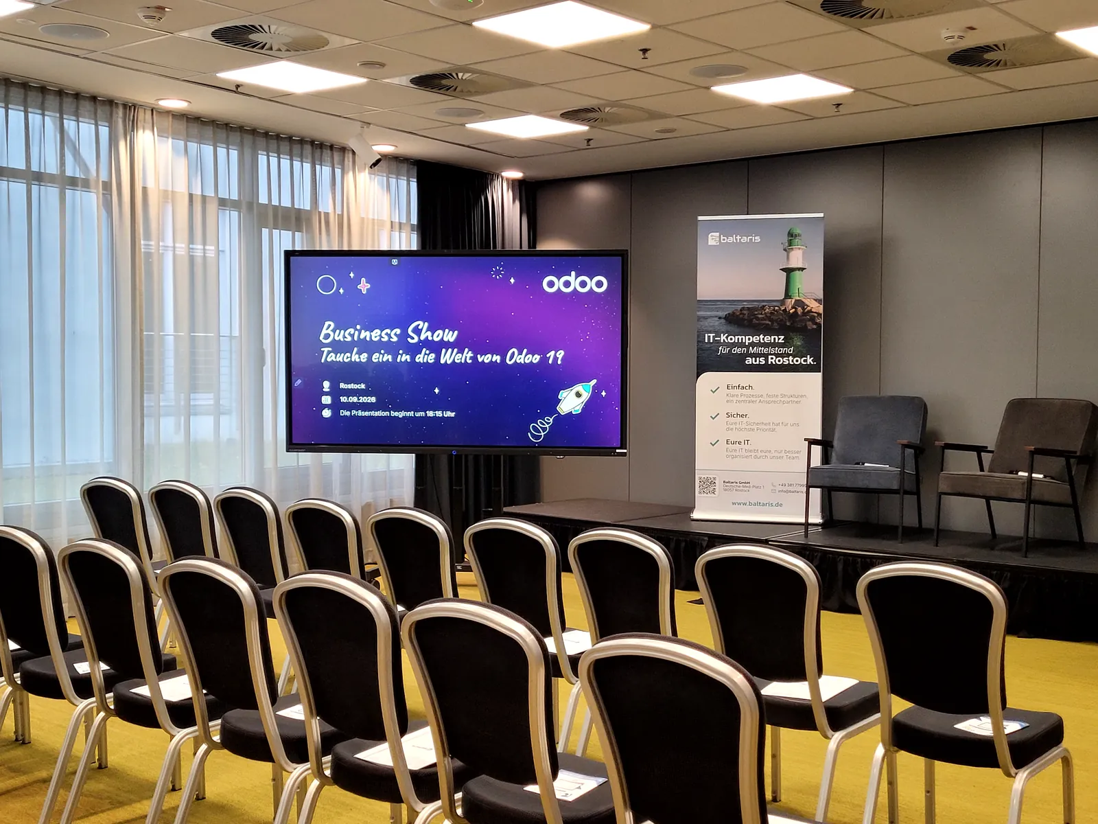 Vor dem Start: die Bühne im pentahotel mit dem Motto des Abends, "Tauche ein in die Welt von Odoo 19", daneben unser Roll-up